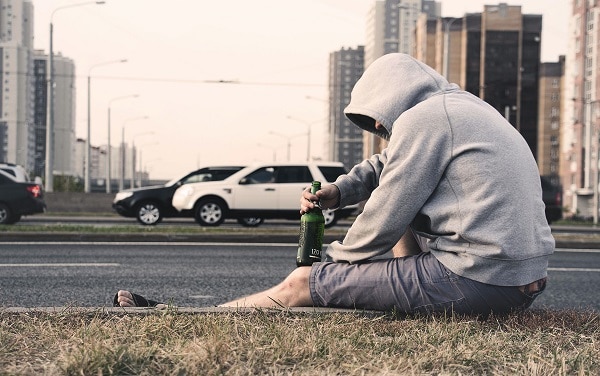 Hombre bebiendo alcohol a la orilla de una carretera