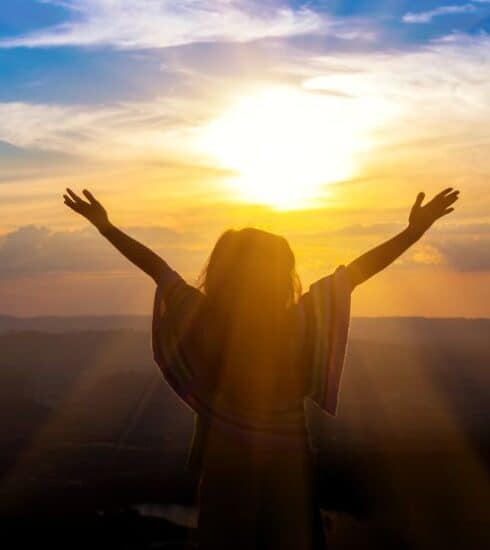 Mujer abriendo sus brazos al cielo en atardecer buscando a Dios