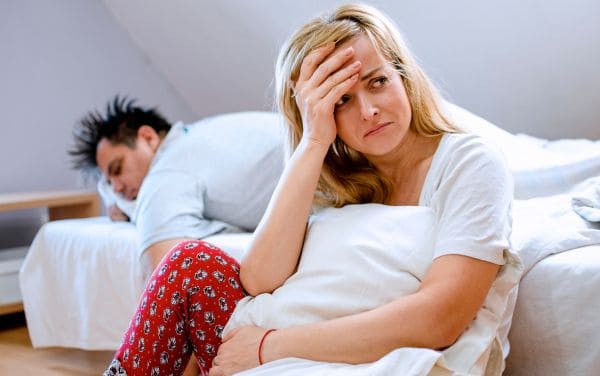 Mujer sentada fuera de la cama sufriendo mientras su esposo duerme