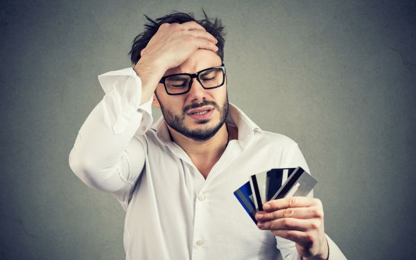 Hombre con las manos en la cabeza mirando sus tarjetas de crédito
